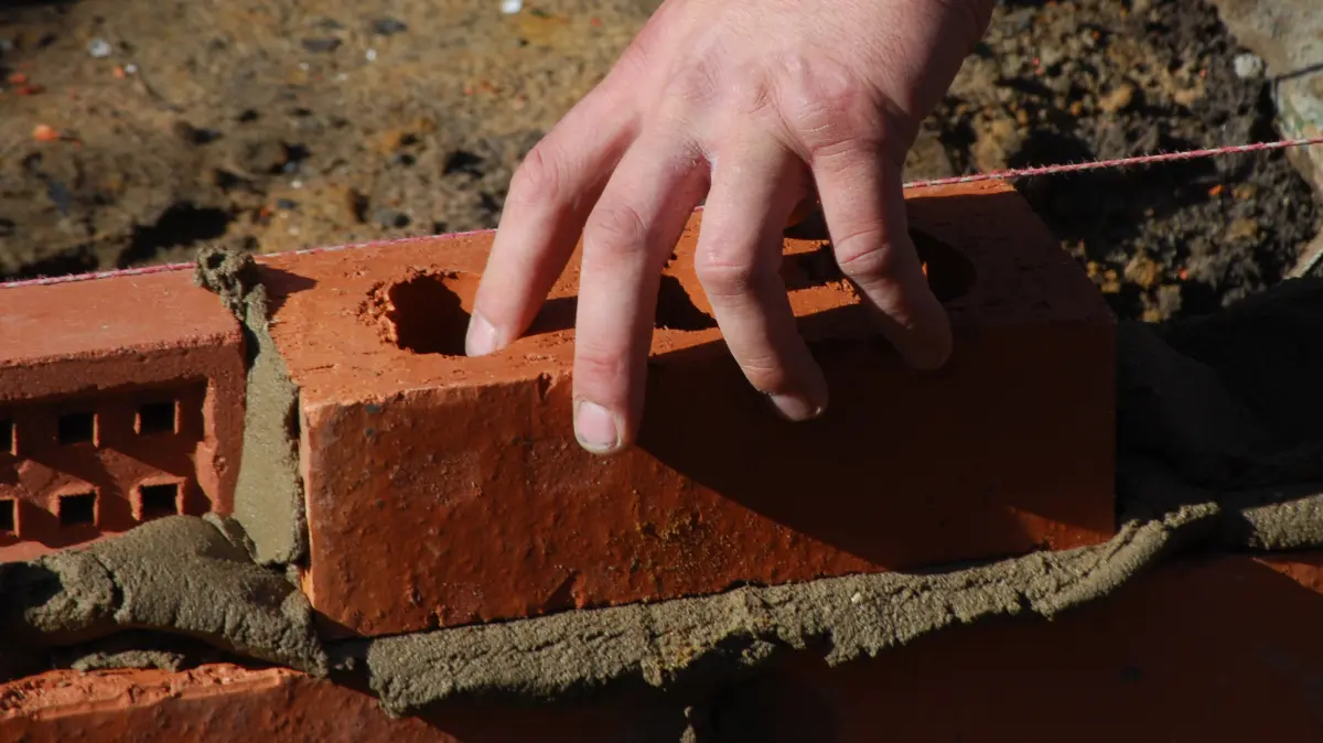 Hand laying bricks on mortar for a wall