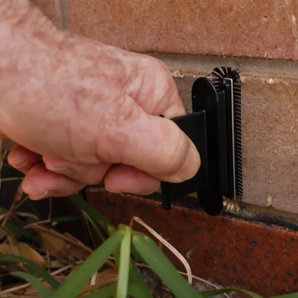 Hand inserting a Weepa Protector Weep Hole Screen into a brick wall.